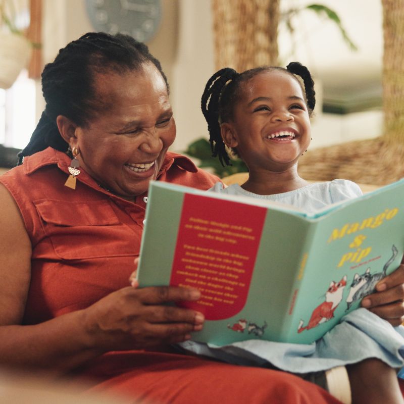 A parent and child sharing a joyful moment while sitting together reading a book, demonstrating positive home reading habits that build early literacy foundations and visual print tracking skills.