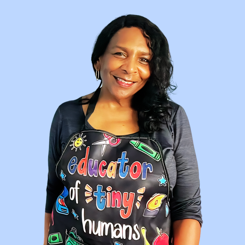 L.T. Lyles, M.Ed., a professional reading specialist and founder of Jumpstart Kinder, smiling warmly in a dark blazer and blue blouse with a soft horizontal blue light glowing behind her.